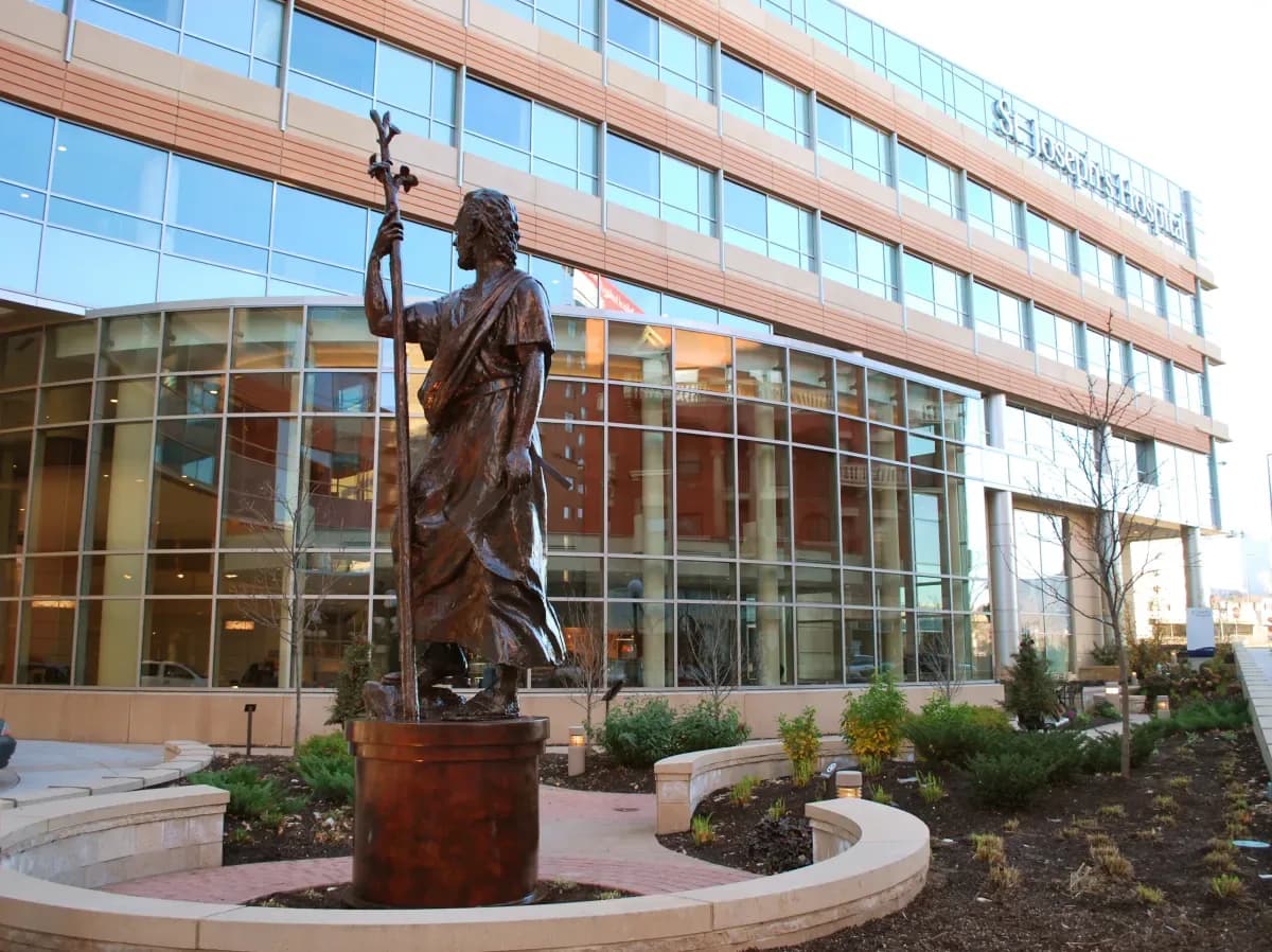Saint Joseph the Worker sculpture — a bronze figure with a flowering staff in a hospital garden