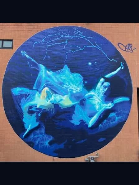 Spirit of the Mississippi, Cyfi's circular mural of two swimmers in deep blue water, painted on a brick wall