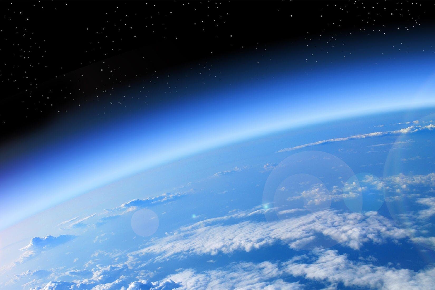 Earth's thin blue atmosphere seen from orbit, clouds below and black space above