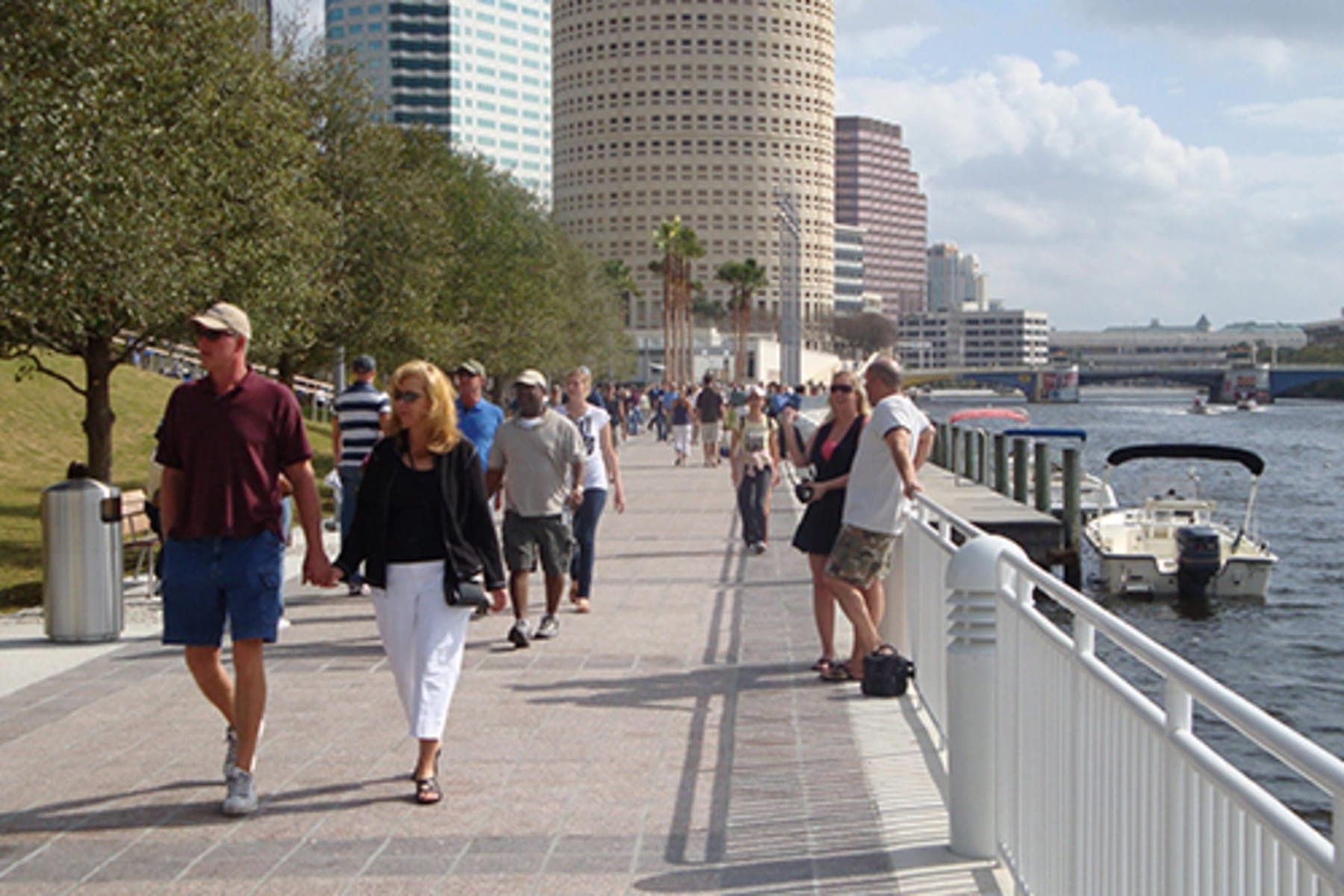 Crowds strolling an early Tampa Riverwalk segment along the Hillsborough River, downtown towers behind