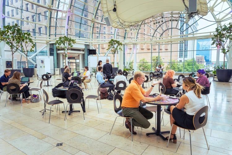 People working and talking at tables under the Artsgarden dome during a Garden Sessions daytime event