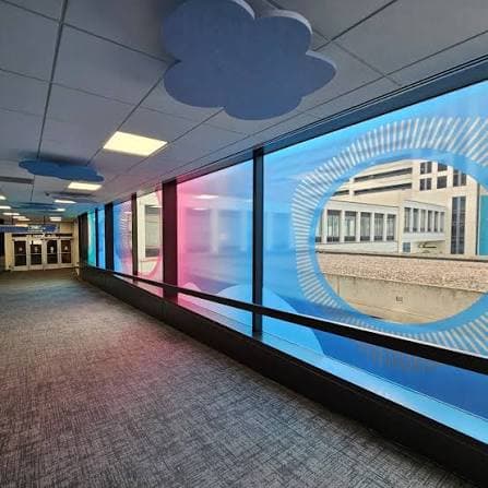 A Des Moines skywalk bridge wrapped in blue cloud window art, with cloud-shaped ceiling panels