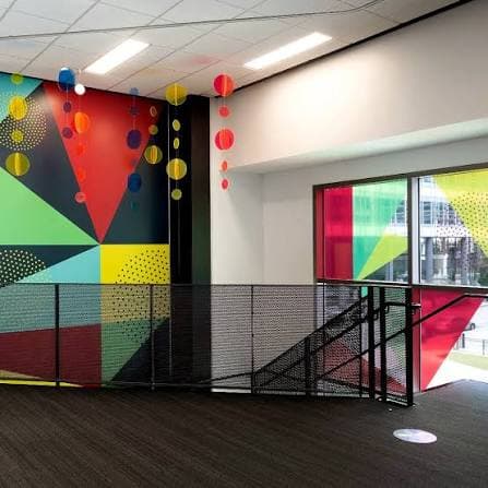 A bold geometric mural and hanging paper lanterns at a Des Moines skywalk stair landing