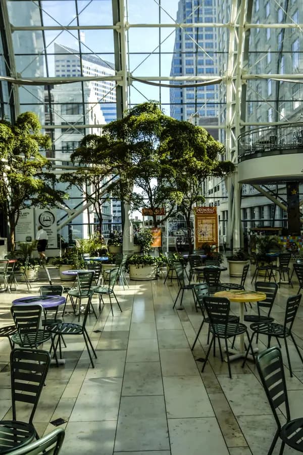 Trees and cafe tables inside the Indianapolis Artsgarden, downtown towers through the glass wall