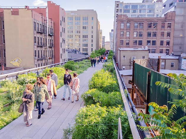 Visitors strolling the High Line's planted walkway between brick buildings