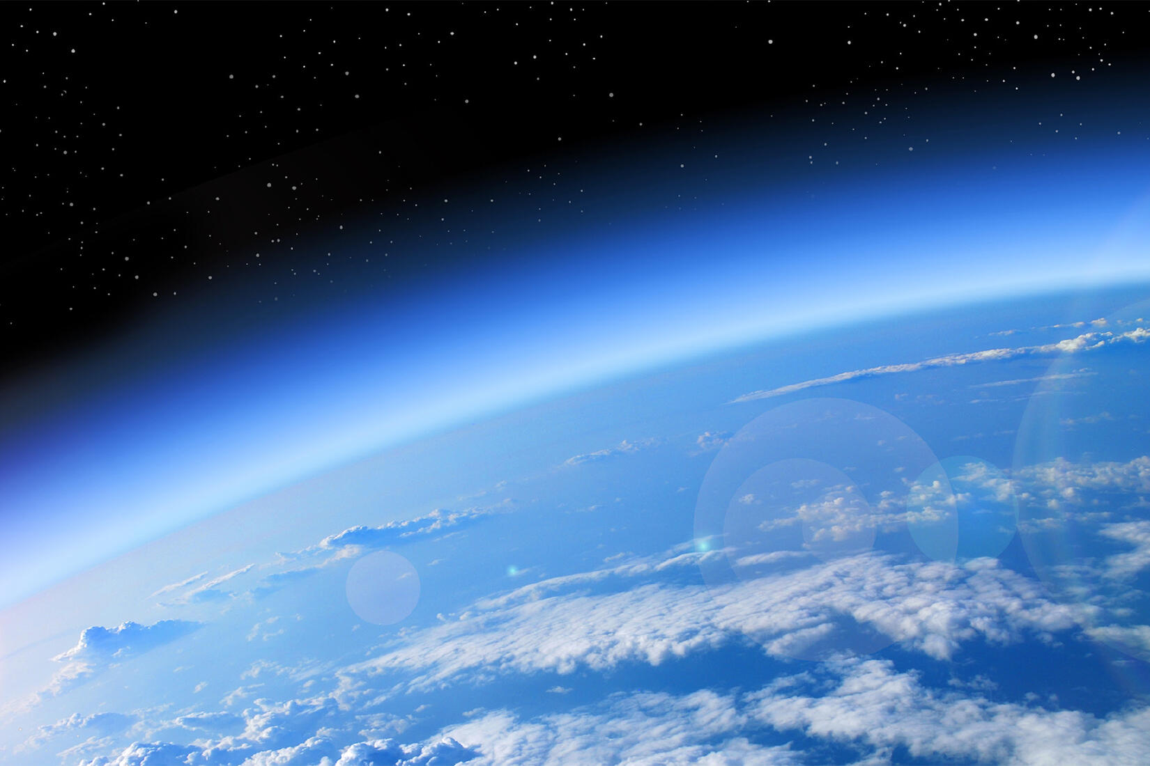 Earth's thin blue atmosphere seen from orbit, clouds below and black space above